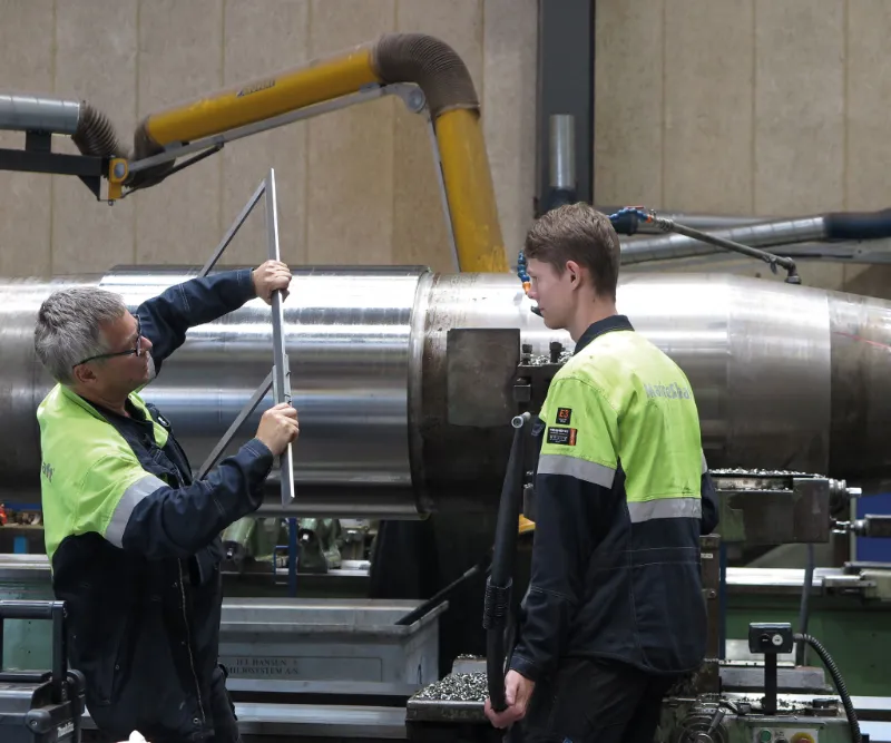 Two technicians measuring a large rudder stock in a lathe