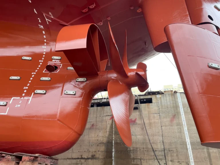 Propeller and rudder bulb on a red hull in drydock